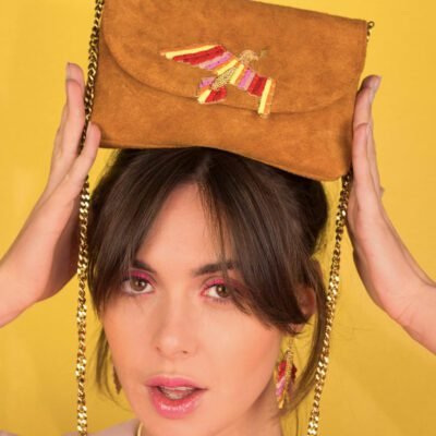 Pochette cuir Colombine | Red Gradiant/Camel Femme brune avec une frange et une chemise robe pâle portant sur sa tête une pochette en cuir camel avec une colombe au centre brodée de fines lanières de cuir de couleur jaune, rose et rouge