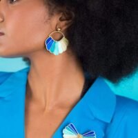 Femme à la peau matte portant sur le col de son blaser bleu une broche brodée de couleur vert et bleu.