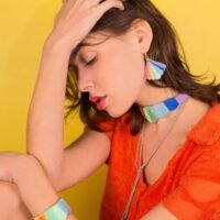 Femme brune assise portant autour de son poignet un bangle brodé à la main de fil de soie couleur arc-en-ciel