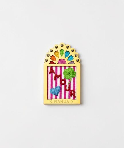 Broche Doriac de la collection Dwara par Nahua, ex-voto doré brodé représentant le mot « Amour », un trèfle vert et un cœur bleu sur fond rayé rose et blanc.
