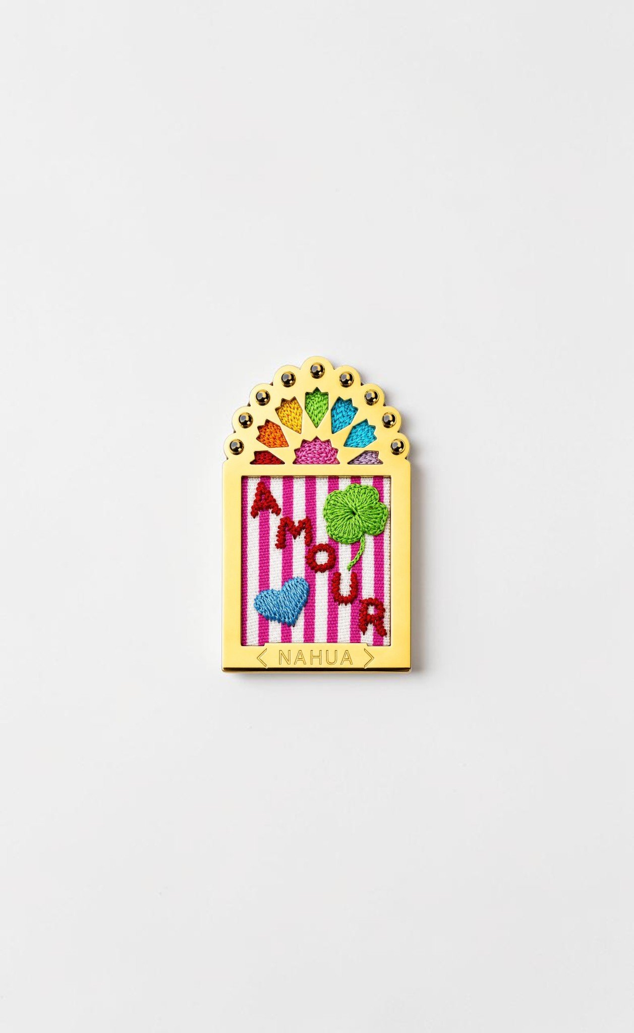 Broche Doriac de la collection Dwara par Nahua, ex-voto doré brodé représentant le mot « Amour », un trèfle vert et un cœur bleu sur fond rayé rose et blanc.