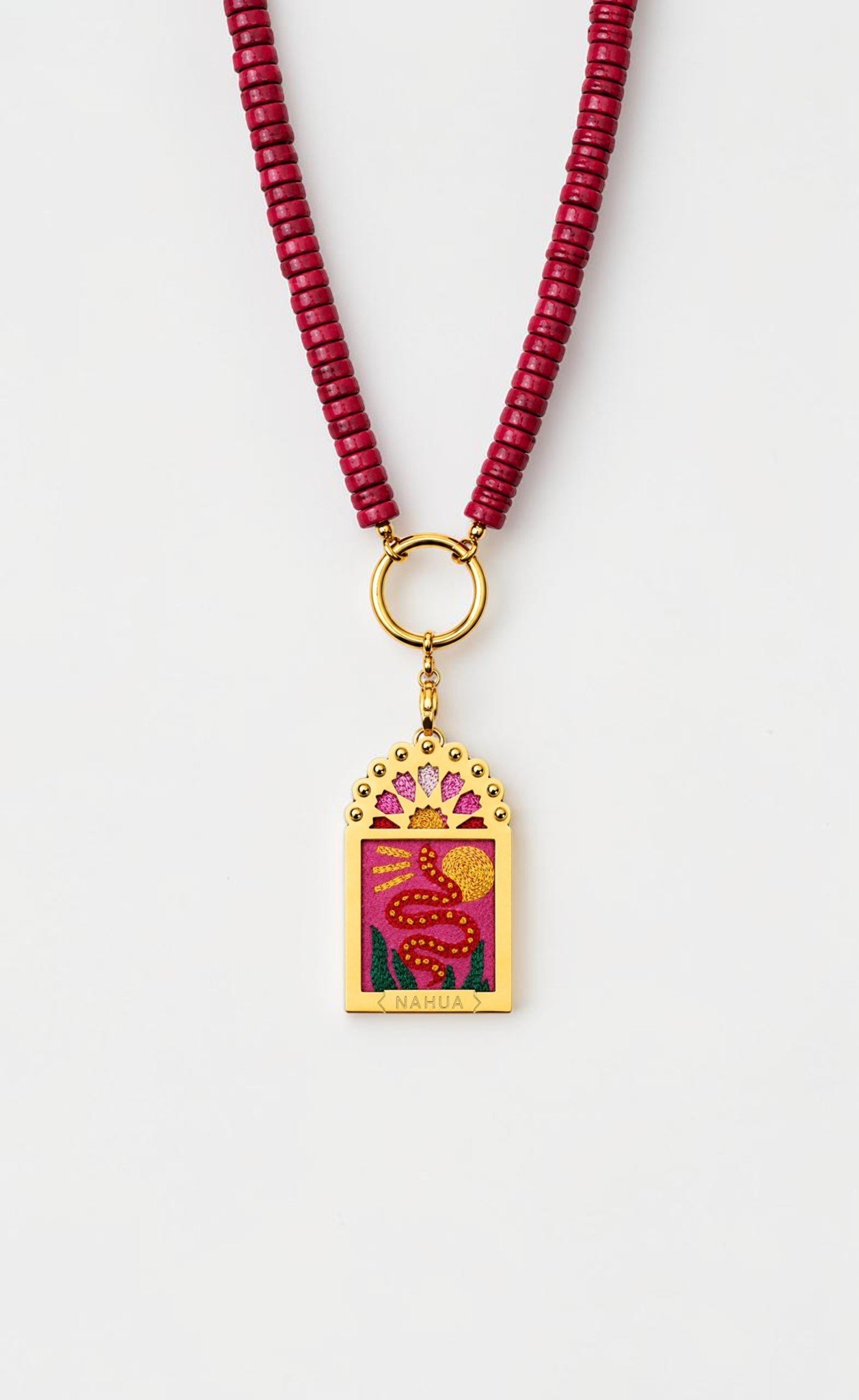 Collier Doriana de la collection Dwara par Nahua, pendentif ex-voto doré brodé représentant un serpent rouge et un soleil doré, monté sur un collier de perles rouges.