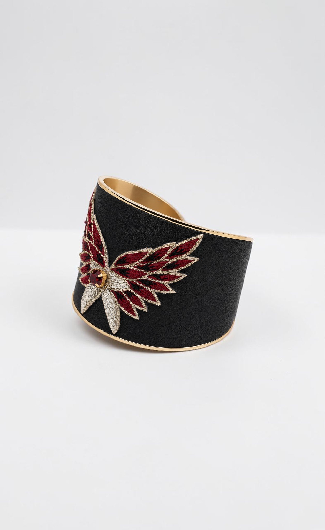 Grand bracelet manchette Glamrock de la collection Glamrock en coloris Burgundy, cuir noir orné d'une broderie d'ailes bordeaux, dorées et noires avec cristal rouge, vue de trois quarts.